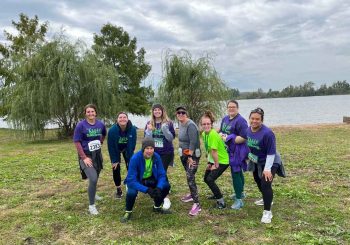 BIFSTL staff group picture at Stampede for Stroke run. 8 people in running gear are posing outside in front of a lake.